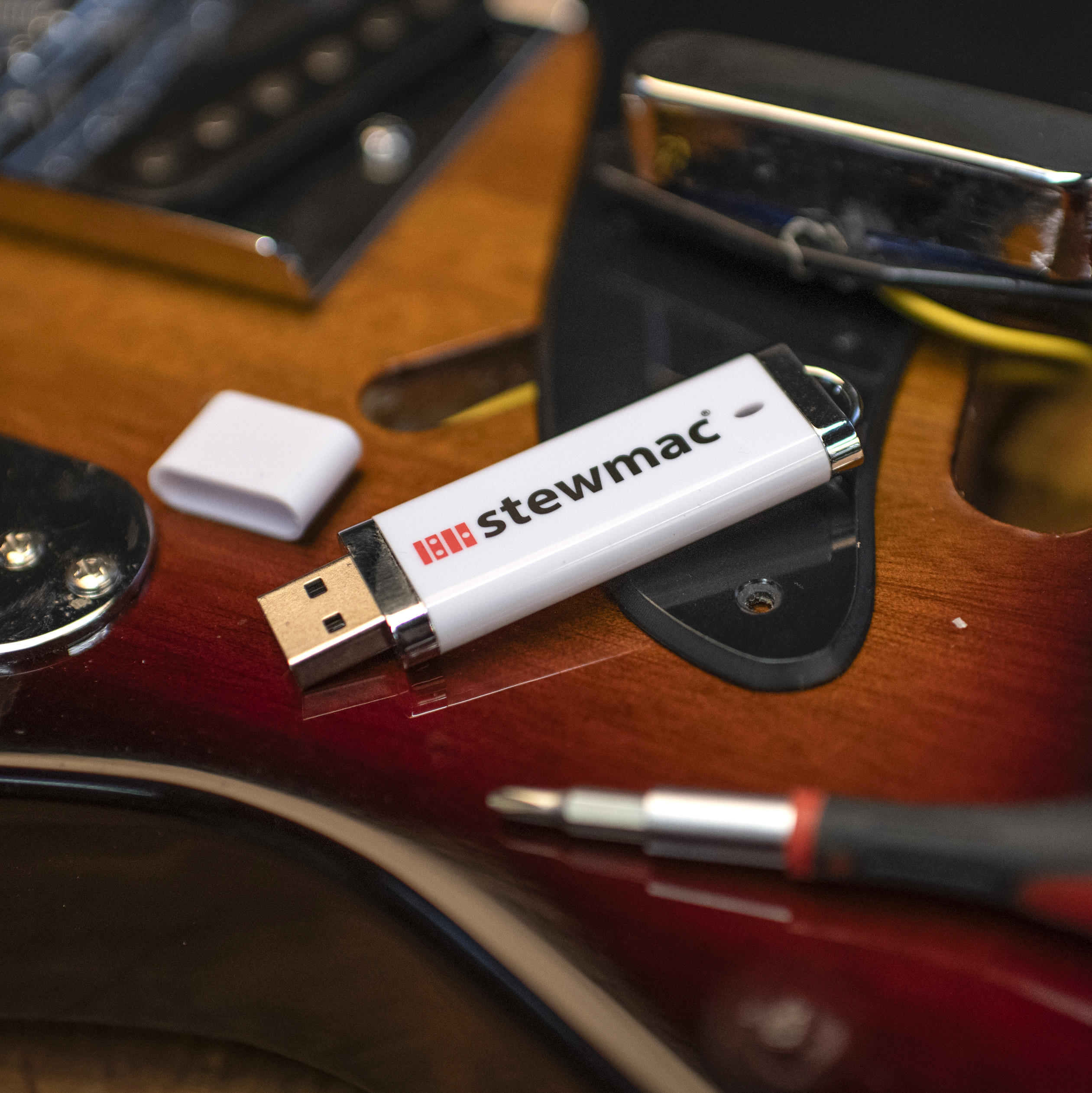 Portable thumbdrive preloaded with StewMac videos on a guitar with luthier tools.